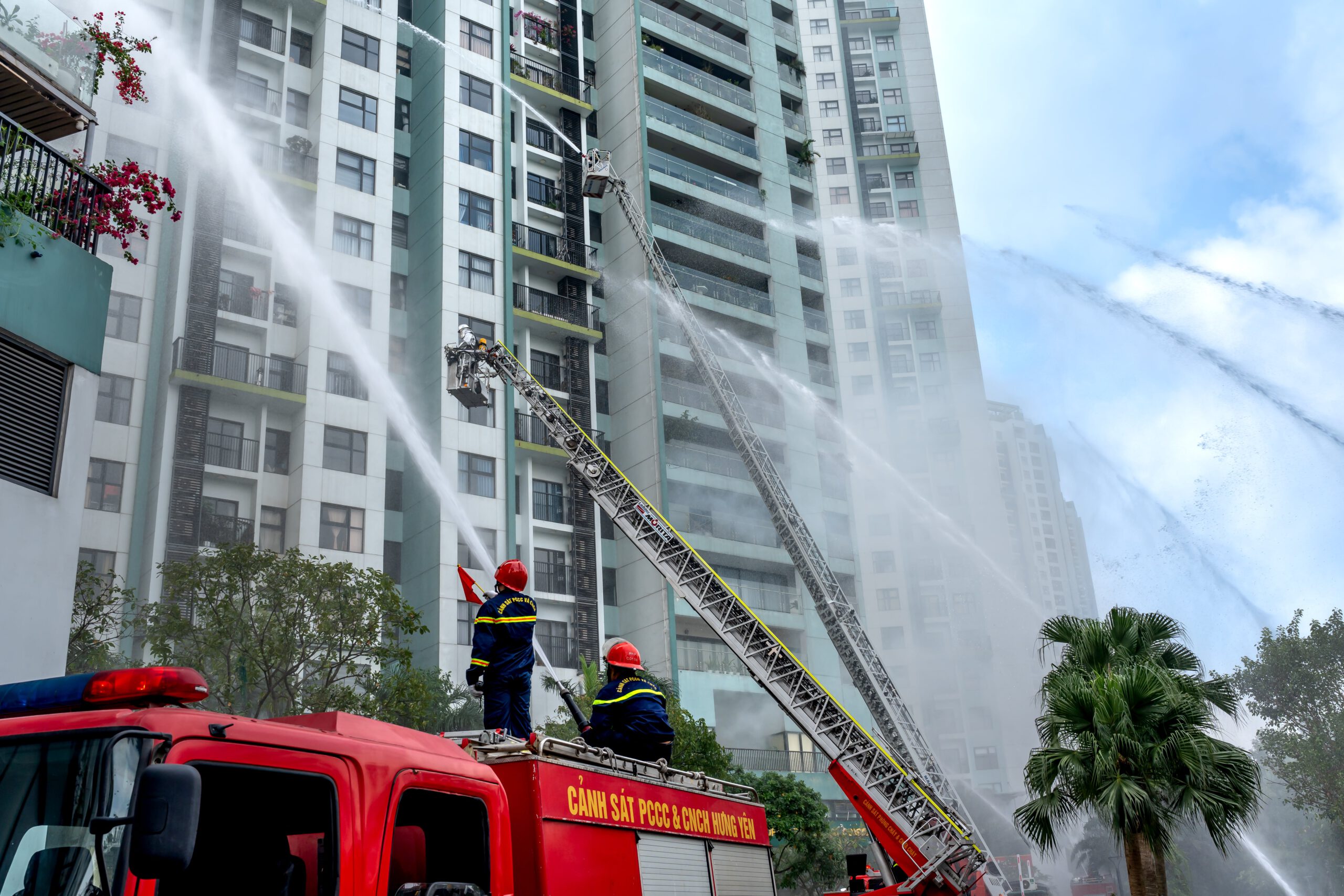 Firemen on Fire Trucks Spraying Water on a High Rises Buildings